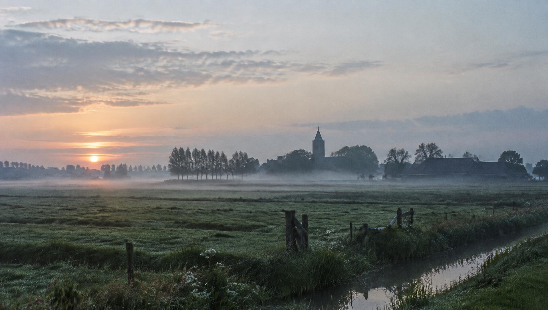De opkomende zon boven het landschap en de kerk van Marum